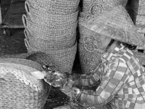 A Vietnamese artisan is painting a hand-woven basket.